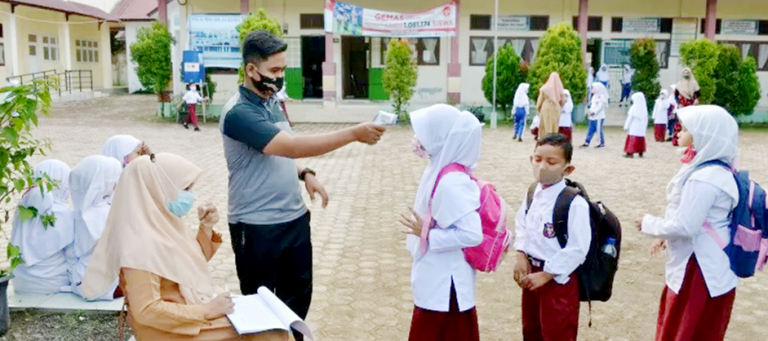 Guru melakukan pengecekan suhu badan dan penggunaan masker murid