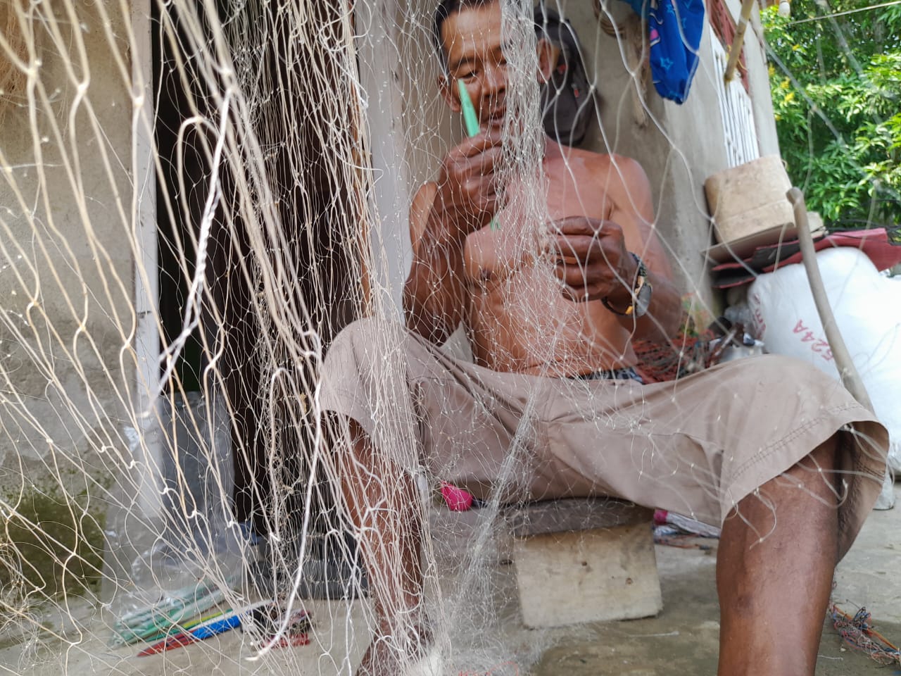 TELATEN : Abah Rita nelayan Kampung Cemara Baru RT (04/32) Kelurahan Palabuhanratu Kecamatan Palabuhanratu, Kabupaten Sukabumi saat memperbaiki jaring yang rusak.