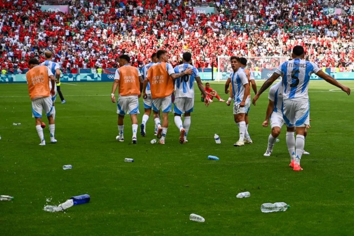 Pemain depan Argentina Giuliano Simeone (kedua dari kanan) melihat botol-botol bekas minuman yang dilemparkan para pendukung Maroko ke lapangan saat pertandingan penyisihan grup B Olimpiade Paris 2024 di Geoffroy-Guichard Stadium, Saint-Etienne, Rabu (24/7/2024). (AFP/ARNAUD FINISTRE)