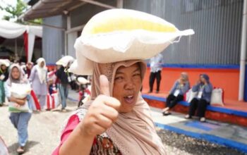 Seorang ibu menjunjung bantuan pangan beras 10 kilogram (kg) sambil mengacungkan jempol. (Humas Bapanas)