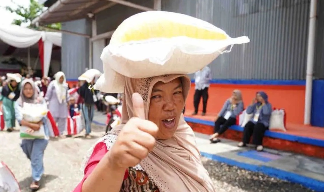 Seorang ibu menjunjung bantuan pangan beras 10 kilogram (kg) sambil mengacungkan jempol. (Humas Bapanas)