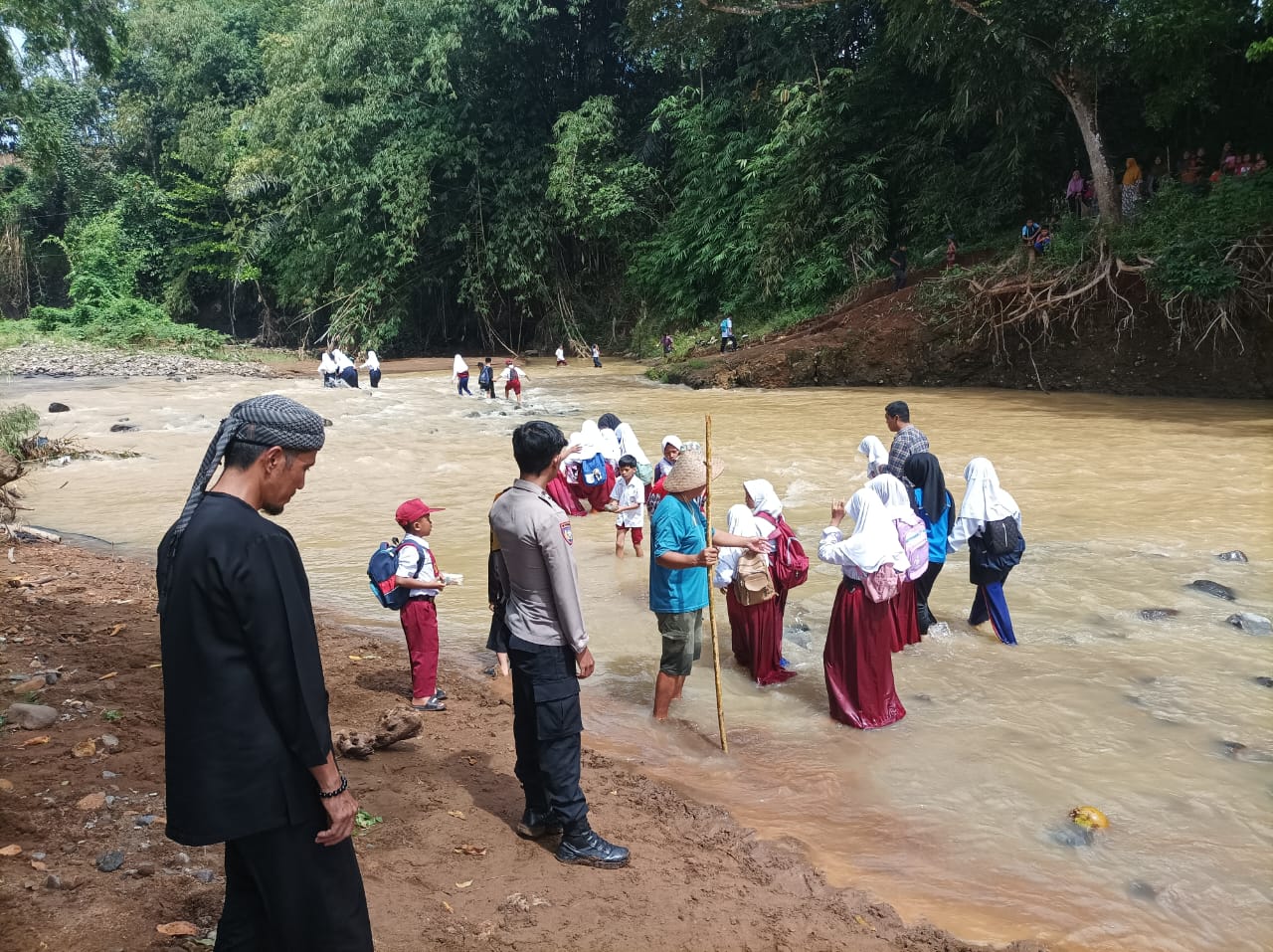 MEMBAHAYAKAN: Sejumlah warga dan anak anak sekolah saat melintasi sungai akibat jembatan hanyut. (Foto: ist)